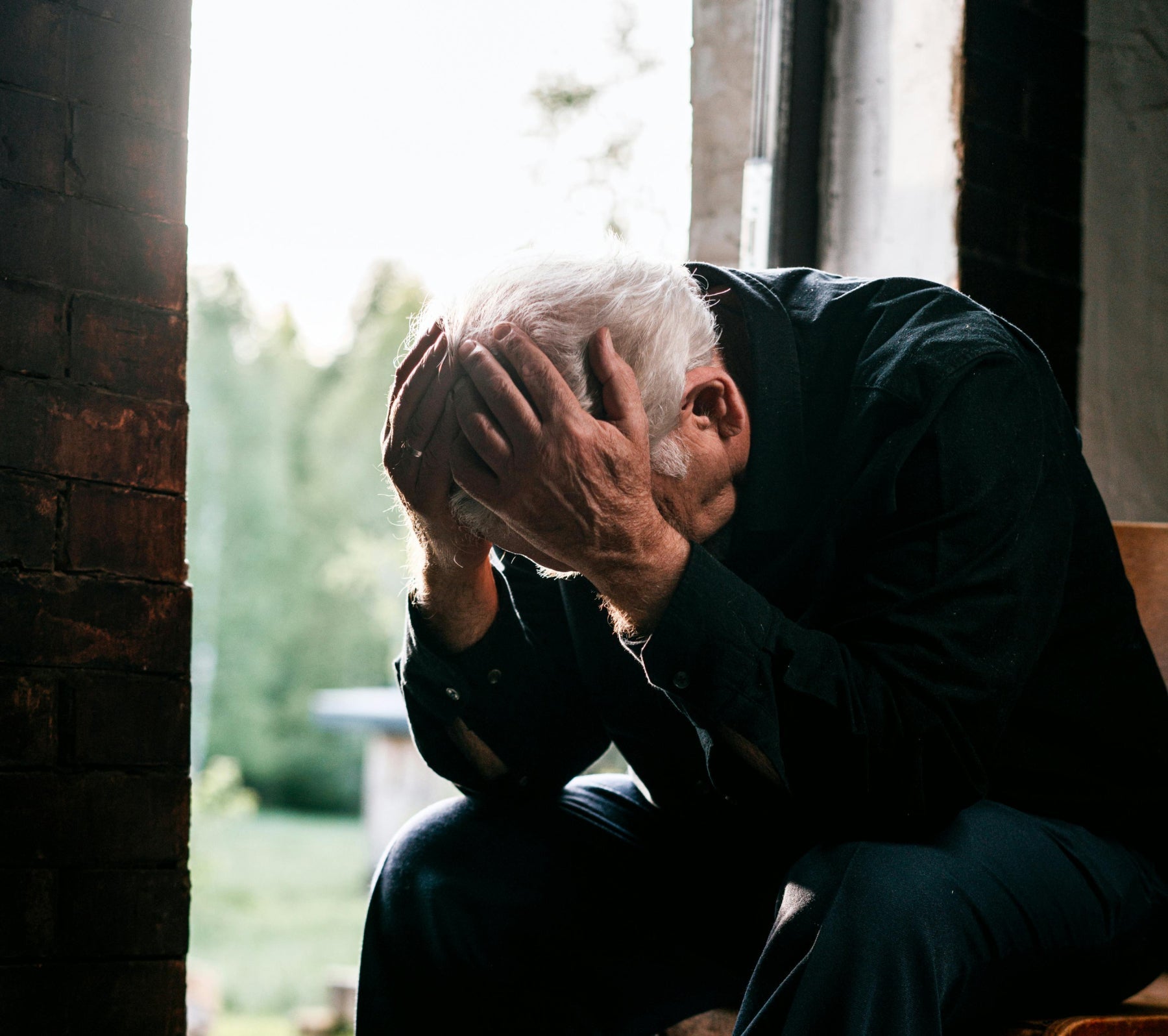 old gentleman all alone in room holding his head in his hands