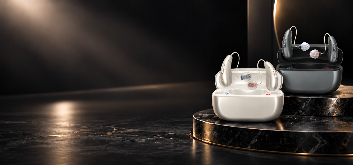 Two pairs of Eara Ascend Premium Bluetooth Hearing Aids with their charging cases displayed on a dark marble pedestal. The foreground case is white with small blue and red accents, and the background case is black with small red and blue accents.slider_item_W4LWgU
