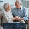 An elderly couple sitting closely together on a couch, smiling and holding hands in a bright living room. The image includes the eara brand logo in the top left and a dark blue feature banner at the bottom with text about warranty, dedicated support, free delivery, and reliability.