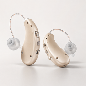 Pair of beige Eara Essential hearing aids with clear tubing and soft ear domes displayed on a neutral background.