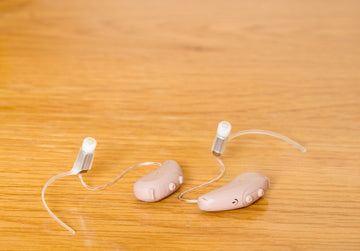 Two beige hearing aids on a wooden surface with concha locks attaced