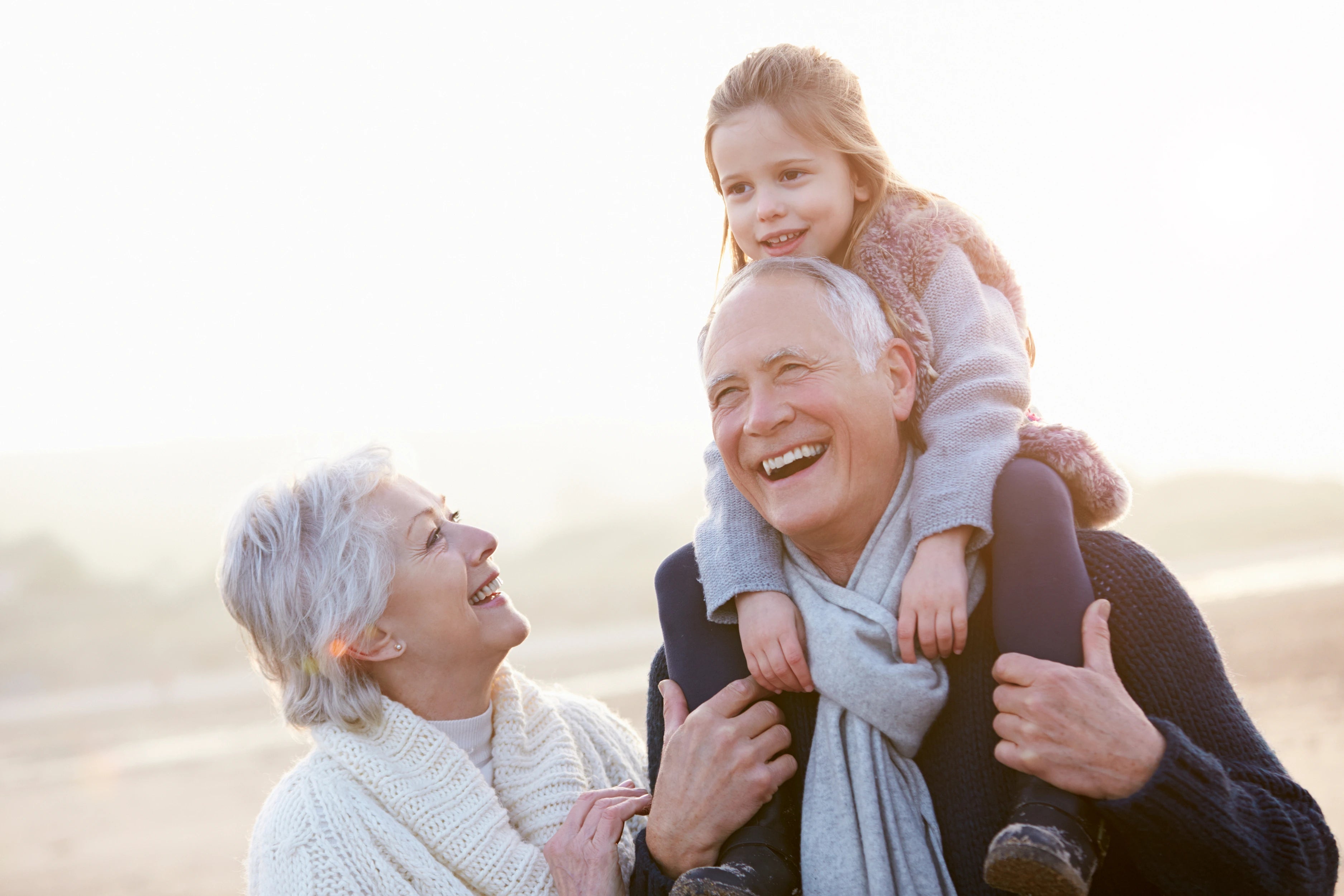 Smiling grandfather carrying granddaughter on his shoulders with grandmother, showing active lifestyle thanks to Eara over the counter hearing aids